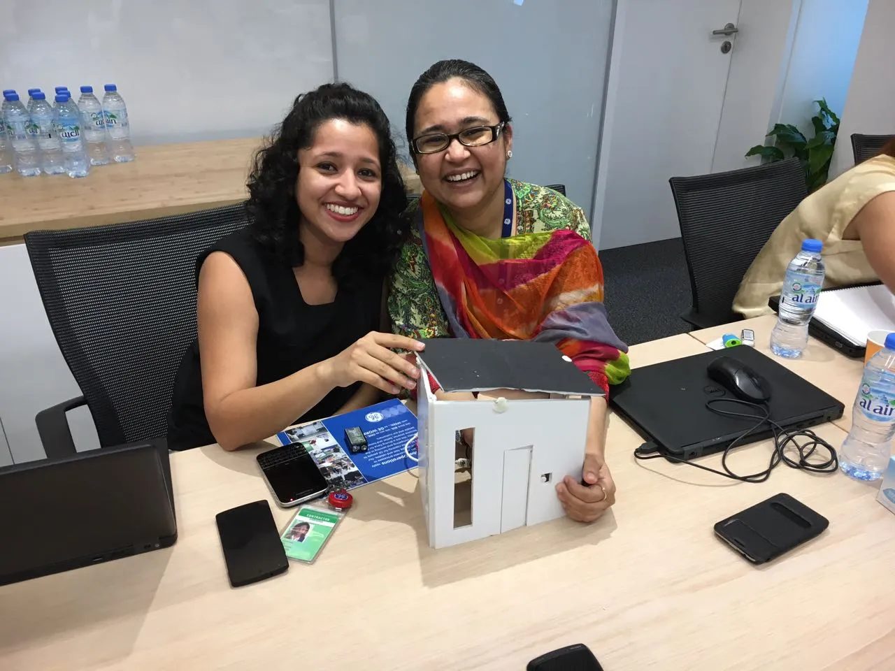 Two General Electric employees smile with the paper house prototype they built during a design thinking workshop