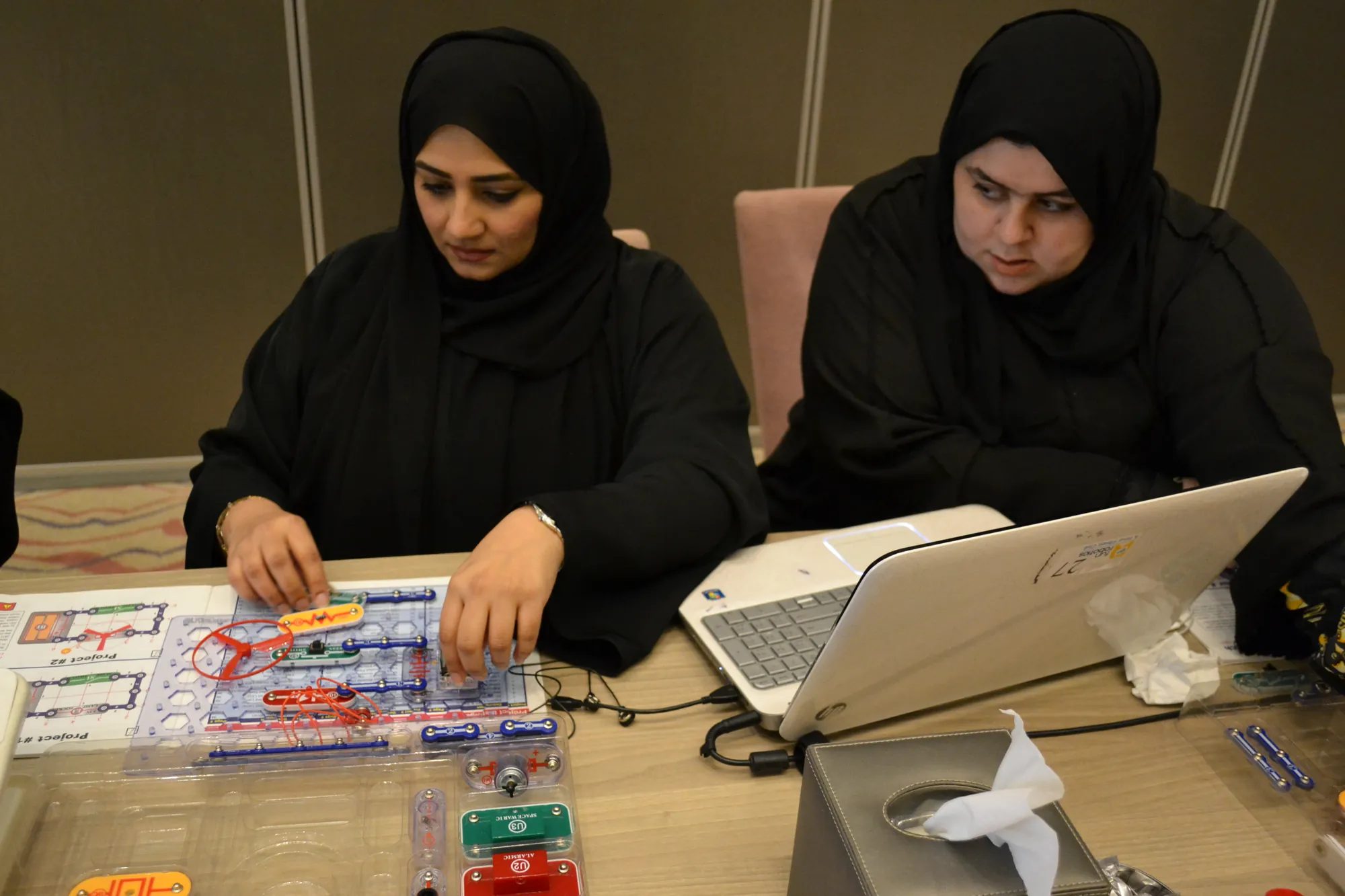 Two women build an electronics circuit with a laptop at a makerspace table during UAE Innovation Week