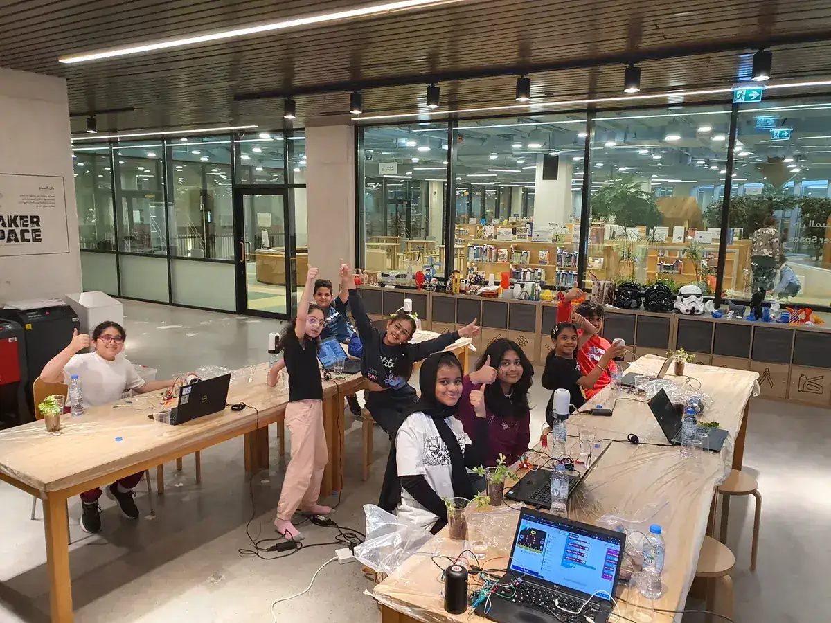 Children cheer at makerspace tables with laptops during a library STEM workshop