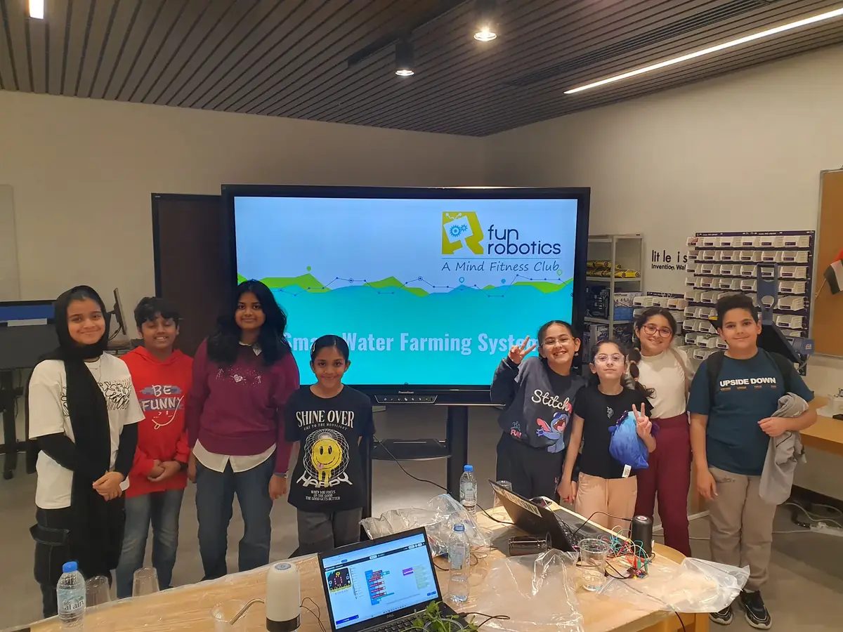 A group of children in a library makerspace in front of a slide about their smart water farming project